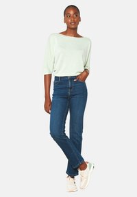 Šviesiai žalia, trumpomis rankovėmis palaidinė su laivų kaklu, derinama su tamsiai mėlynomis aukštu liemeniu džinsais ir baltais sportbačiais su spalvingais akcentais.