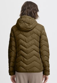 Būdos žalios spalvos paminkštintas švarkas su gaubtu, pasižymintis chevron raštu ir elastinėmis rankogaliais. Lygios tekstūros, laisvo stiliaus, be matomos aparatūros.