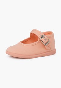 Zapato de tela color durazno con punta redondeada, estilo Mary Jane, que lleva una correa con hebilla y una suela de goma flexible. Textura suave en general.