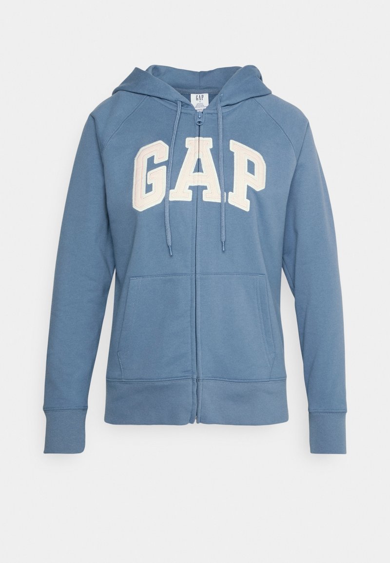 Felpa blu con zip realizzata in tessuto morbido, dotata di tasca a marsupio e grande logo bianco "GAP" sulla parte anteriore, con cappuccio regolabile tramite lacci.