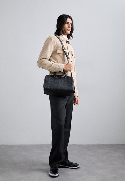 Borsa in pelle nera con motivo testurizzato, manici superiori e tracolla staccabile. Abbinata a un giacca in corduroy beige e pantaloni neri.