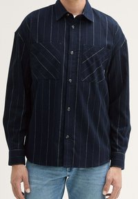Camicia button-up blu navy con righe verticali bianche, due tasche sul petto e colletto classico. Realizzata in tessuto texturizzato.