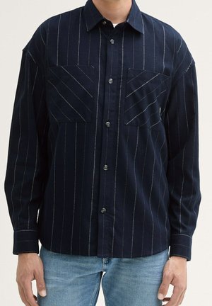 Chemise bleu marine à boutons avec des rayures verticales blanches, deux poches poitrine et un col classique. Fabriquée en tissu texturé.
