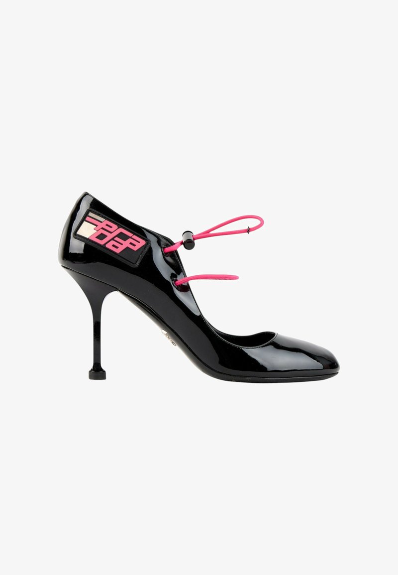 Escarpin en cuir verni noir à talon haut fin, lacets élastiques roses et patch logo rose et noir près du talon.