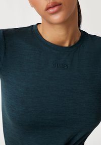 Teal fitted t-shirt gemaakt van zachte stof, met een subtiele textuur en een gegraveerd "GUESS" logo op de borst. Ronde halslijn, korte mouwen.