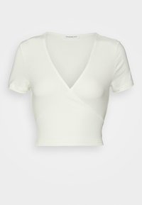 Crop top blanc à manches courtes avec un décolleté en V profond façon cache-cœur, en tissu doux et extensible.