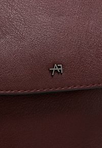 Borsa in pelle color bordeaux con finitura testurizzata, caratterizzata da un piccolo logo metallico nell'angolo e cuciture a contrasto lungo il bordo.