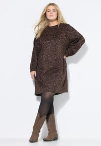 Bruine panterprint jurk met lange mouwen en een relaxte pasvorm, gecombineerd met bruine cowboylaarzen en zwarte maillot. Minimale accenten, gestructureerd materiaal.