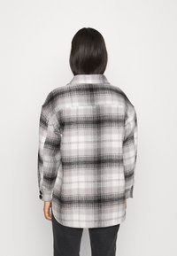 Plaid shirt jacket in black and white tones, featuring a soft fabric, buttoned cuffs, and a classic collar. Standard cut, no additional details.