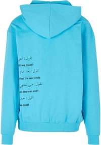 Sudadera azul claro con cordón, con texto negro en varios idiomas en la parte posterior. Material de algodón suave con puños acanalados.