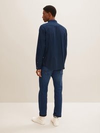 Marineblauses Hemd mit langem Arm und Standardkragen, kombiniert mit mitteldunkelblauen Jeans und weißen Sneakers. Glattes Material mit figurnaher Passform.