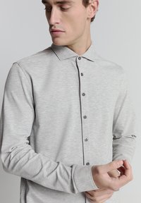 Lichtgrijs overhemd met lange mouwen en een button-down kraag, voorzien van donkere knopen en een gladde textuur. Slim fit met op maat gemaakte manchetten.