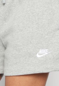 Shorts en coton gris avec une texture douce et une taille élastique, arborant un logo Nike blanc brodé sur le bas à gauche.