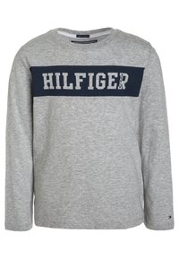 Harmaa pitkähihainen paita, joka on valmistettu puuvillasta. Paidassa on laivastonsininen nauha, jossa on suuret valkoiset kirjaimet "HILFIGER" rinnan kohdalla. Klassinen pyöreä kaula-aukko.