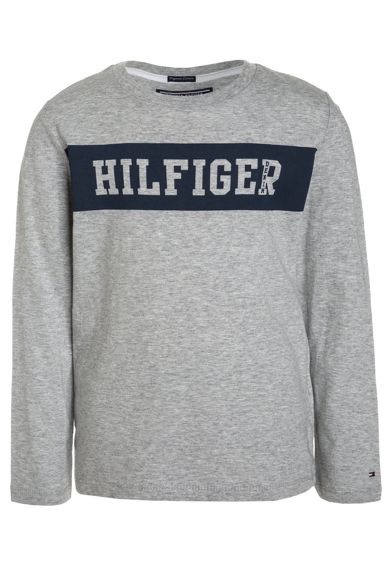 Harmaa pitkähihainen paita, joka on valmistettu puuvillasta. Paidassa on laivastonsininen nauha, jossa on suuret valkoiset kirjaimet "HILFIGER" rinnan kohdalla. Klassinen pyöreä kaula-aukko.