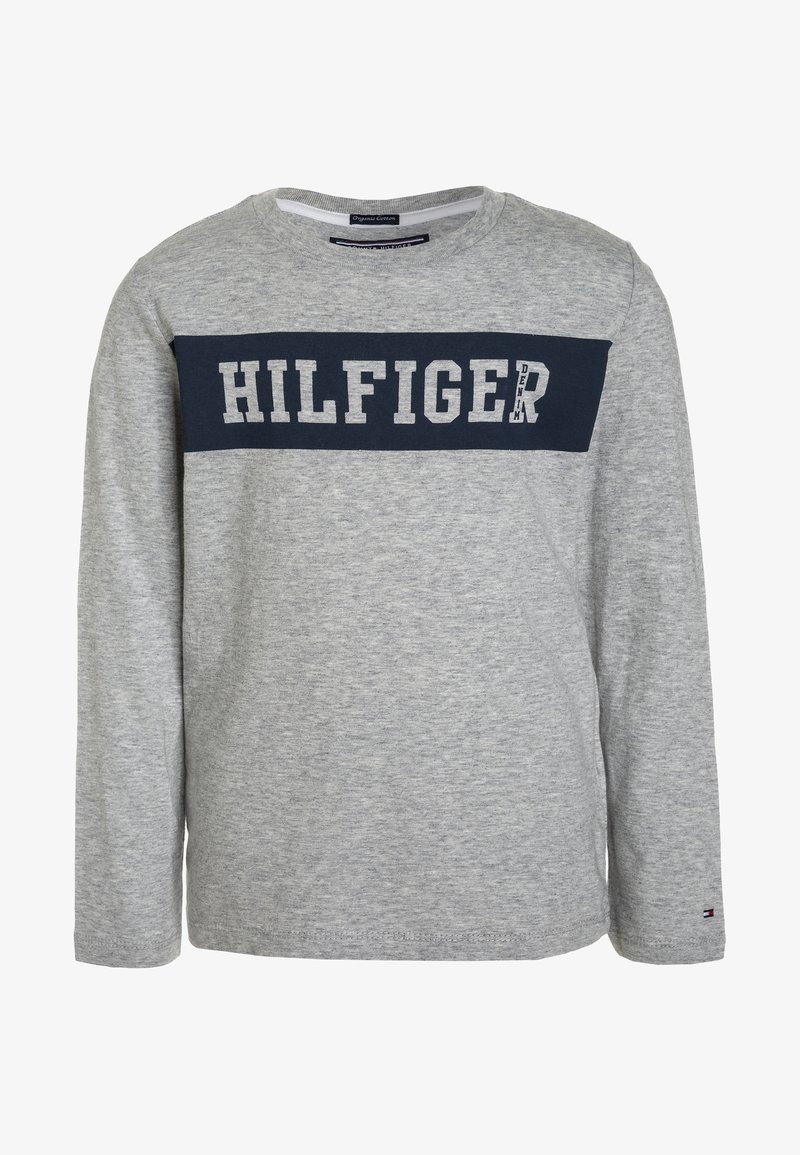 Harmaa pitkähihainen paita, joka on valmistettu puuvillasta. Paidassa on laivastonsininen nauha, jossa on suuret valkoiset kirjaimet "HILFIGER" rinnan kohdalla. Klassinen pyöreä kaula-aukko.