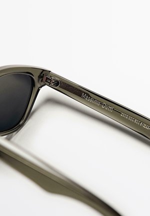 Sonnenbrille mit dunklen Gläsern und olivgrünen Kunststoffrahmen. Metallbeschläge mit eingraviertem Branding. Glatte Textur mit glänzendem Finish.