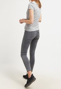 Camiseta gris de manga corta combinada con pantalones vaqueros ajustados grises y zapatillas negras. El conjunto presenta un diseño simple sin patrones ni acentos.