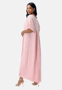 Robe longue rose ample en tissu texturé, avec manches courtes et encolure dégagée. Associée à des sandales à talons hauts roses.