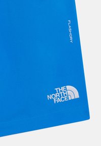 Tissu bleu au toucher lisse, avec la marque blanche "THE NORTH FACE" et "FLASHDRY" imprimée de manière proéminente.