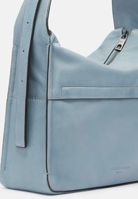 Borsa a spalla in pelle azzurro chiaro con chiusura a zip, cuciture in evidenza e tasca frontale. Texture liscia e tracolla regolabile.