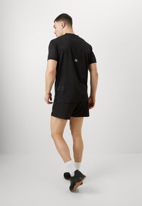 Μαύρο αθλητικό μπλουζάκι με κοντά μανίκια, πλέγμα υφής και λογότυπο στην πλάτη. Φοριέται με μαύρη βερμούδα και αθλητικά παπούτσια.