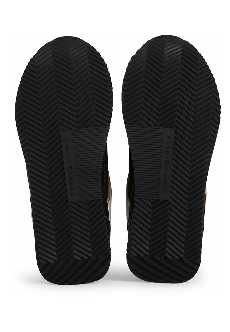 Suela de zapato de goma negra con un patrón de espiga y el logo en relieve "TOMMY HILFIGER", con lados texturizados para mayor agarre y soporte.