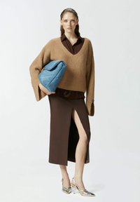 Maglione marrone a maglia con scollo a V, abbinato a una gonna marrone con uno spacco laterale. Borsa a tracolla blu imbottita e scarpe con tacco alto metalliche.