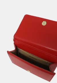 Portafoglio rosso in pelle con una texture liscia, hardware tono oro, chiusura a scatto e un compartimento etichettato all'interno. Forma rettangolare compatta.