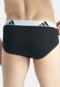 Svarta bomullskalsonger med ett vitt elastiskt midjeband som har tre svarta remsor och en slät yta, som visar en figursmickrande design.