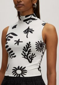 White sleeveless top with high collar, featuring black abstract floral and leaf patterns. The fabric has a ribbed texture.
