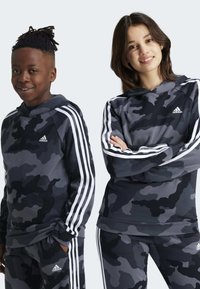 Felpe camouflage nere e grigie con strisce bianche sulle maniche. Caratterizzate da un tessuto morbido e una vestibilità comoda, indossate da due persone.