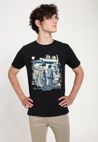 Černé bavlněné tričko s vintage potiskem v modré barvě, zobrazující postavy poblíž vlaku označeného "Clipper" s stylizovanými akcenty.