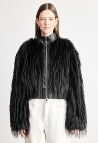 Jaqueta cropped em pele sintética preta com detalhes em couro, apresentando um colarinho alto, fecho de correr e mangas longas e desgrenhadas. Design texturizado e ousado.