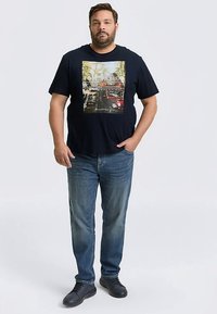 Marineblaues T-Shirt mit kurzen Ärmeln und fotografischem Grafikdruck. Kombiniert mit hellblauen Jeans und schwarzen Schuhen.
