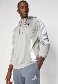Grå hættetrøje med hvide side striber, prydet med "Olympique Lyonnais" logo. Sammen med grå bukser med Adidas-logo.
