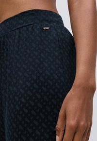 Sorte mønstrede bukser med en blød tekstur, der har en bred talje og en lille metallisk logo detalje på siden.