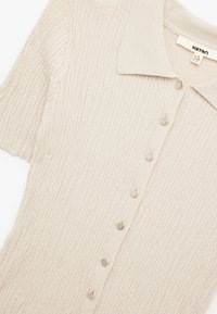 Lichtbeige cardigan met ribbeltextuur, een kraag, en zes metalen knopen aan de voorkant, gemaakt van een zachte, gebreide stof.