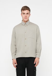 Ανοιχτό γκρι μακρυμάνικο πουκάμισο με κολάρο, κουμπιά μπροστά και μία τσέπη στο στήθος. Υφή υφάσματος και καφέ κουμπιά.