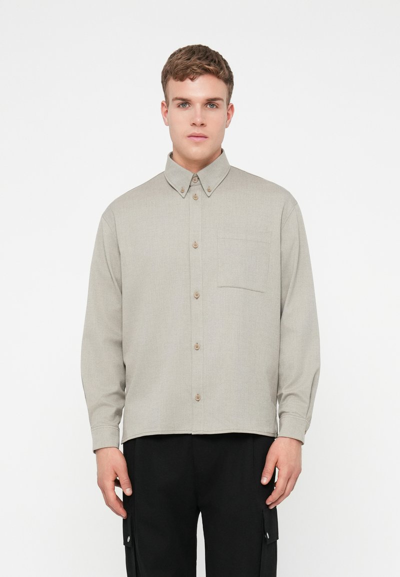 Ανοιχτό γκρι μακρυμάνικο πουκάμισο με κολάρο, κουμπιά μπροστά και μία τσέπη στο στήθος. Υφή υφάσματος και καφέ κουμπιά.