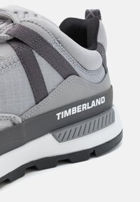 Pelēkie sporta apavi ar sietu un sintētiskiem materiāliem, ar melniem akcentiem, teksturētu zoli un "TIMBERLAND" zīmolu uz papēža.