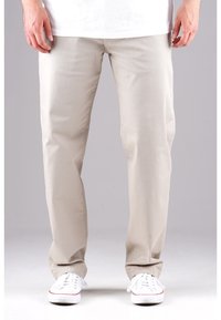 Beige Baumwollhosen mit geradem Bein, seitlichen Taschen und subtiler Textur. Kombiniert mit weißen Sneakers mit farbigen Akzenten.