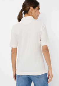 Hvid polo t-shirt med korte ærmer, glat tekstur, foldede manchetter og en klassisk krave. Bæret med blå denim jeans.