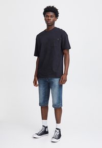 T-shirt noir à manches courtes avec une poche, associé à un short en denim et des baskets montantes noires. Design simple, coupe décontractée et tissu texturé.