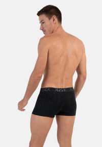 Boxer aderenti neri realizzati in materiale morbido con un elastico decorato, caratterizzati da una vestibilità attillata e una trama liscia, mostrati da un'angolazione posteriore.