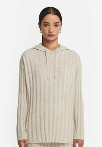 Jasnobeżowy, prążkowany hoodie z długimi rękawami, przednią kieszenią kangurką oraz regulowanymi sznurkami na kapturze. Przyjemny w dotyku, miękki materiał.