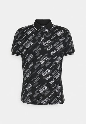 Camiseta tipo polo negra con el texto "Versace Jeans Couture" y "Since 1988" impreso en diagonal por toda la prenda, con cuello y puños ribeteados en blanco.