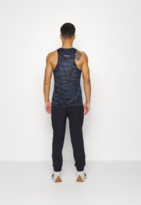 Black tank top with a wavy pattern, worn with dark joggers and white sneakers featuring green and brown accents.