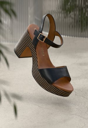 Sandales à plateforme en cuir noir avec un strap à la cheville à boucle, présentant un talon tissé texturé et une semelle intérieure lisse marron.