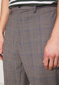 Hnědé kostkované kalhoty s mixem malých vzorů a modrých akcentů; vyrobené z texturované látky se štíhlým střihem; knoflík v pase.